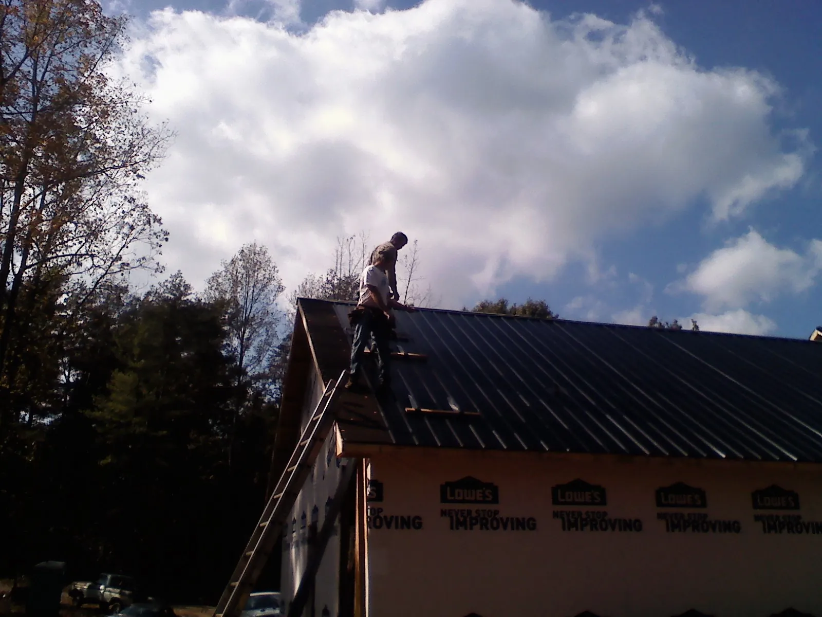 Roofer fastening dark metal panels high against a cloudy sky, from a Roof Inspection job in District Heights