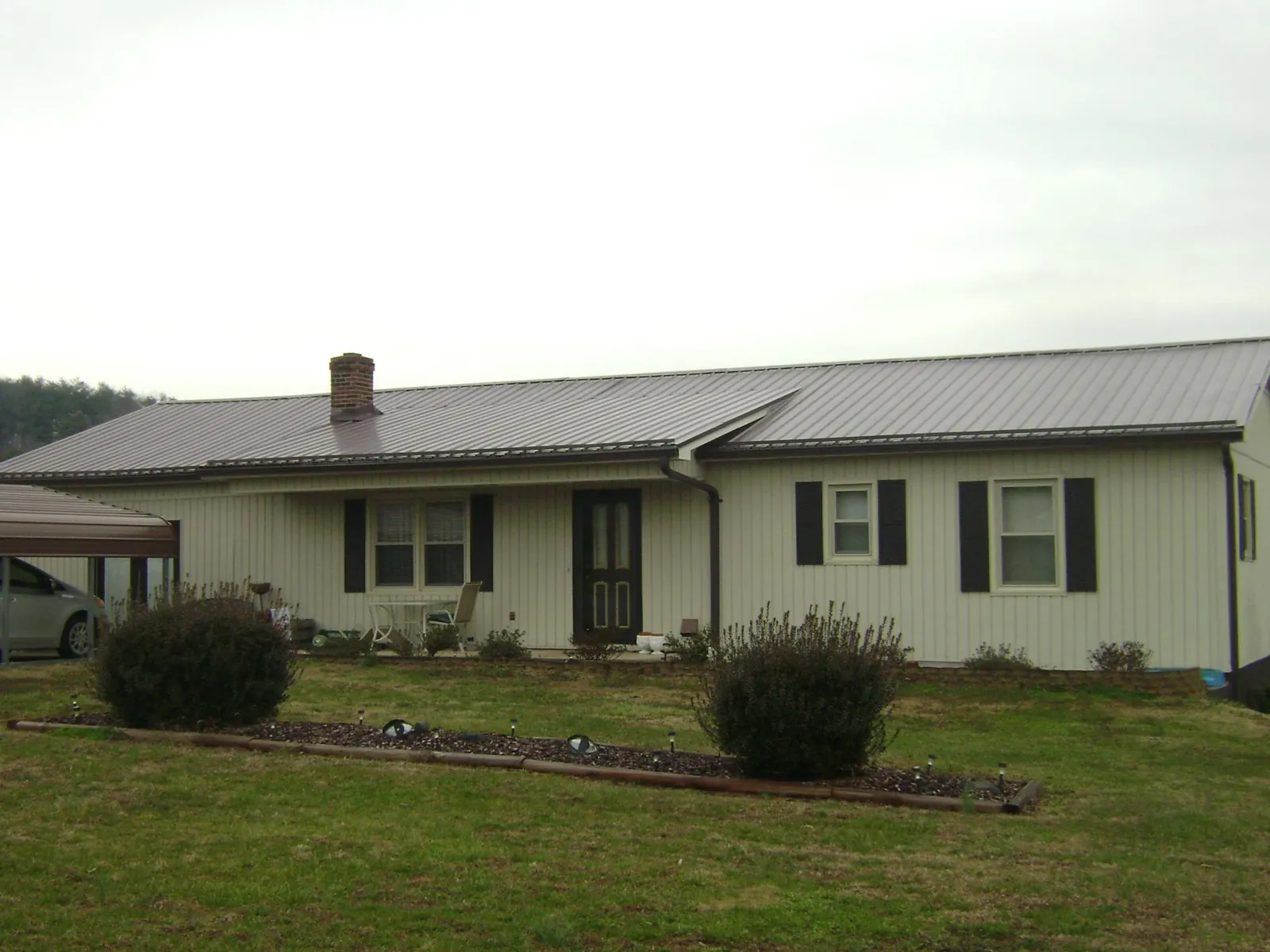 Brown metal roof on a cream sided ranch home with a brick chimney in District Heights